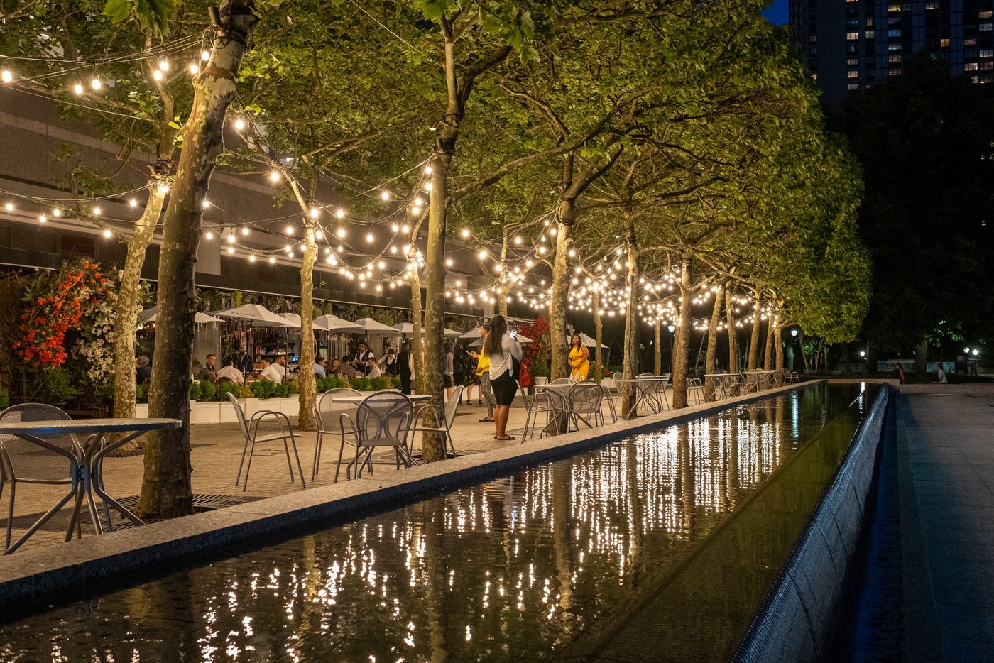 Waterfront terrace under trees lit with string lights in the evening, New York