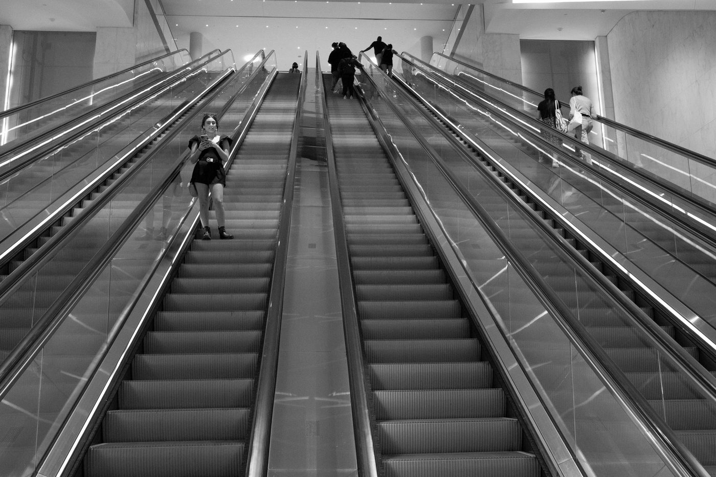 Young woman on her phone going down an escalator between symmetrical lines, New York