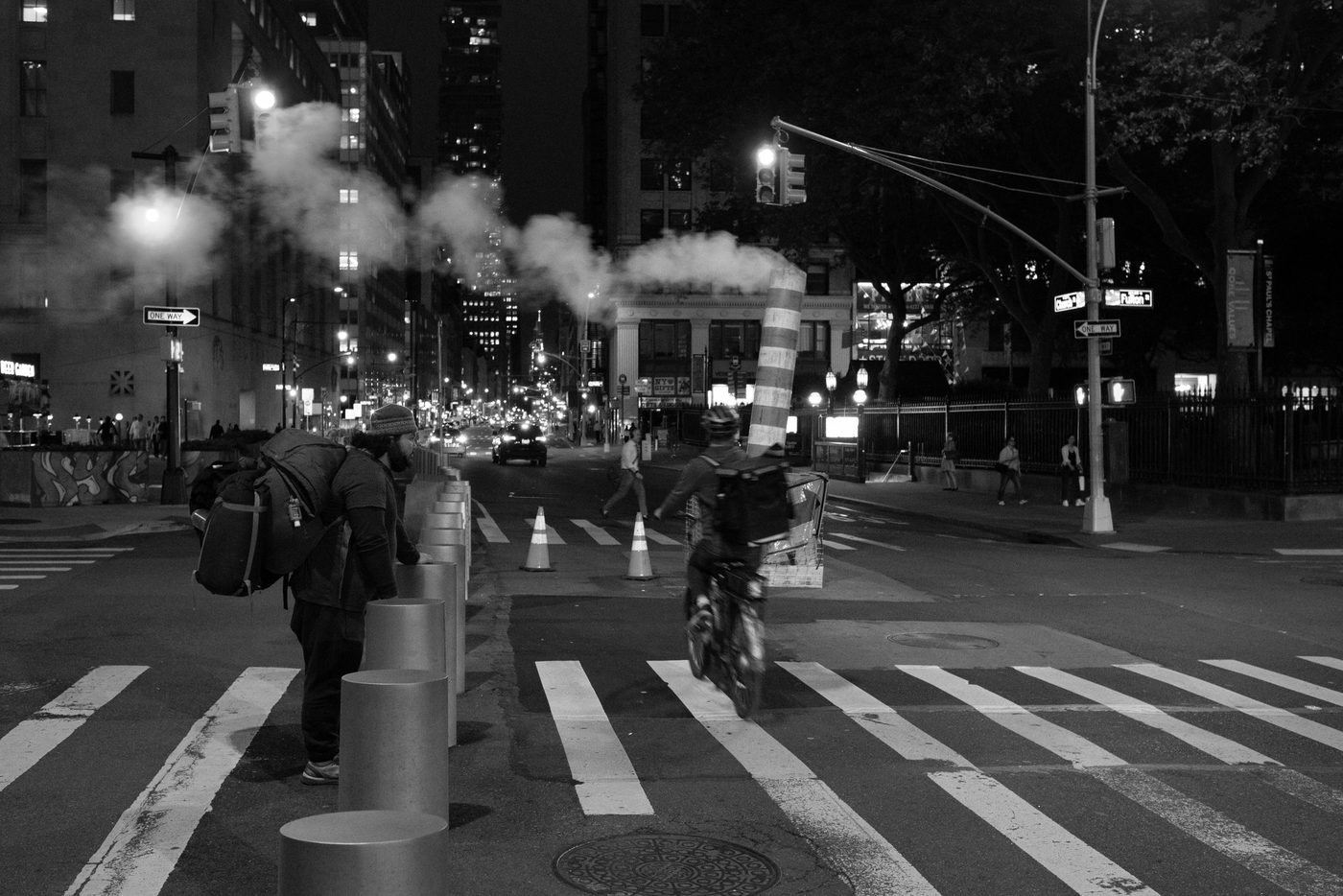Steam rising from the asphalt at night as a delivery cyclist crosses the street, New York