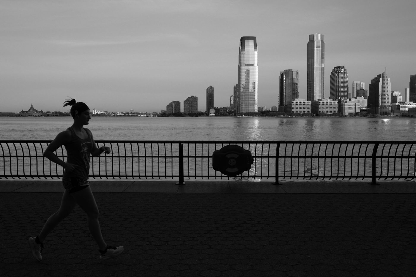 Silhouetted female runner along the promenade facing the skyscrapers, New York