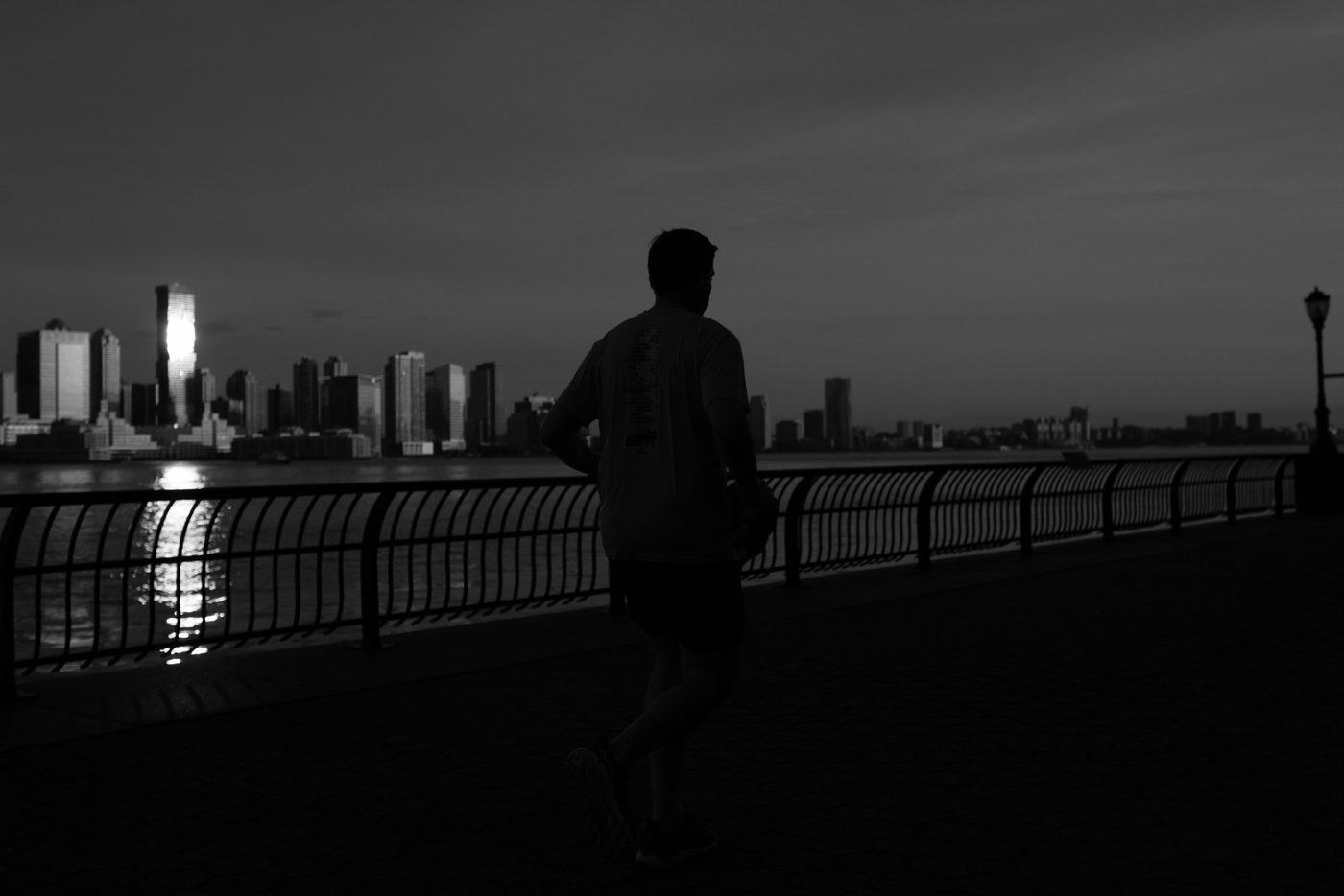 Runner seen from behind at dusk facing the skyline reflected on the water, New York