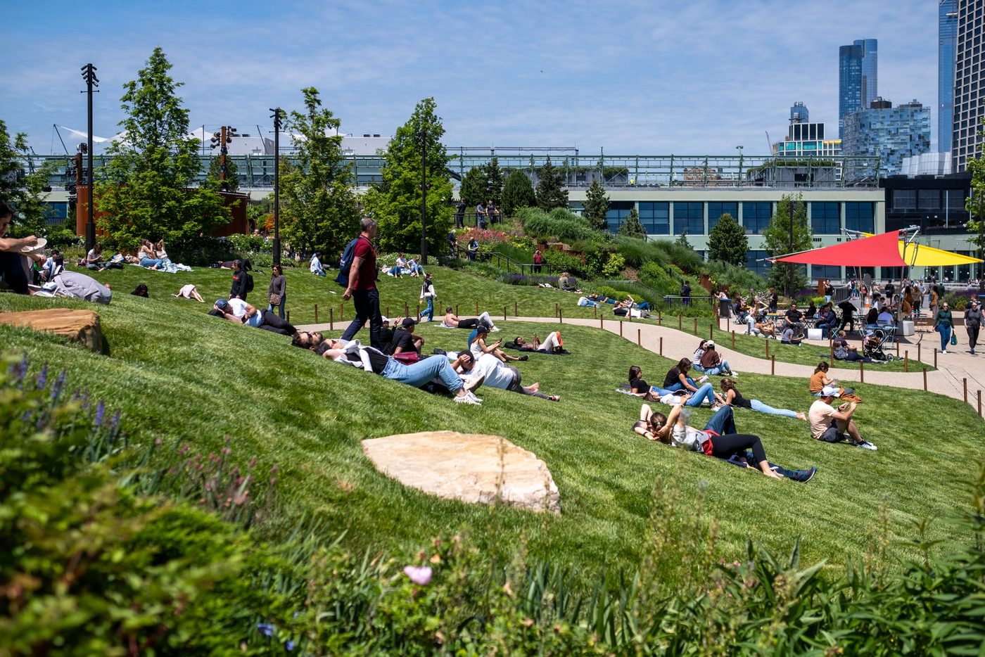 Visitors lying on the sloped lawn of Little Island, skyline in the background, New York