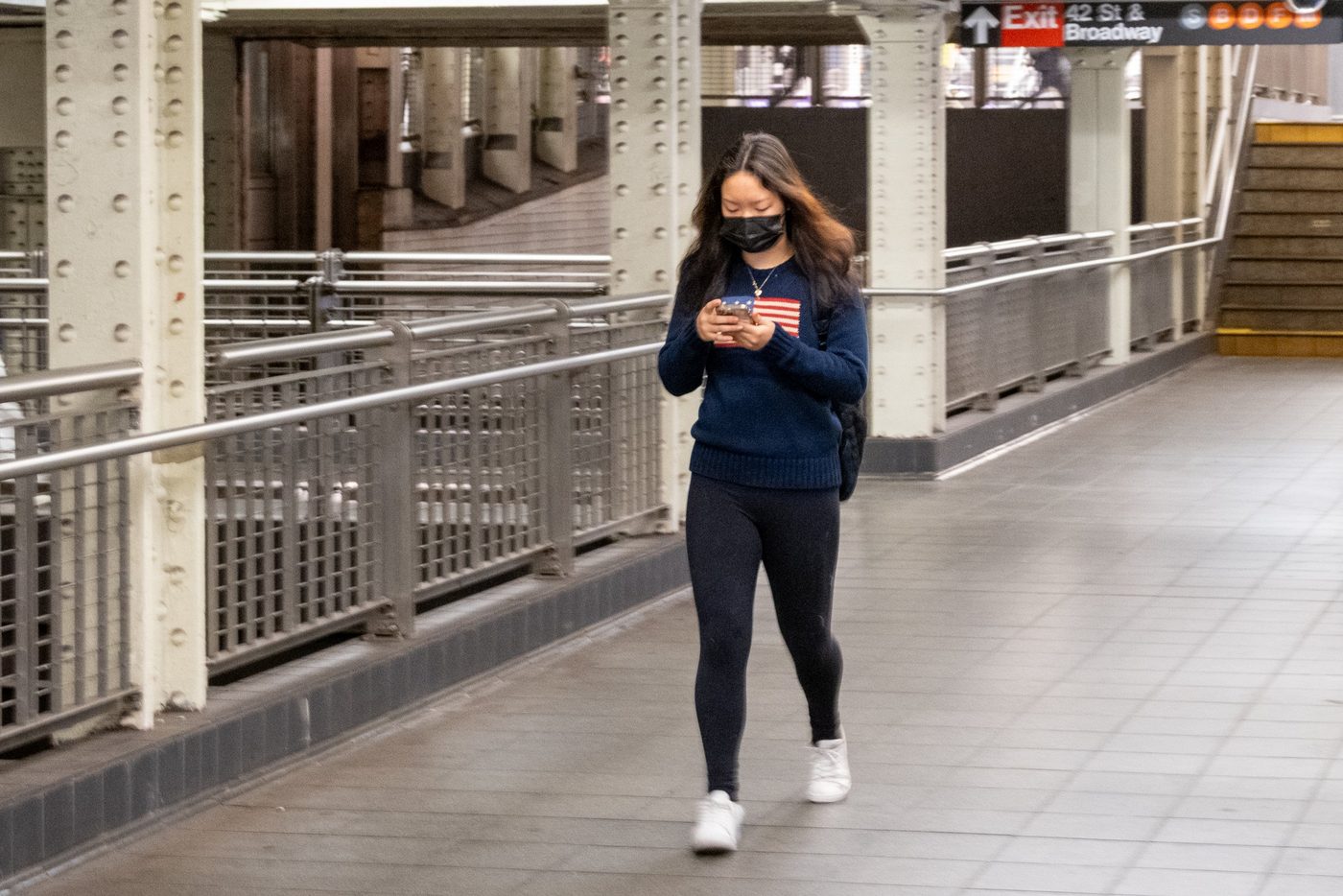 Masked young woman checking her phone in a subway corridor, New York