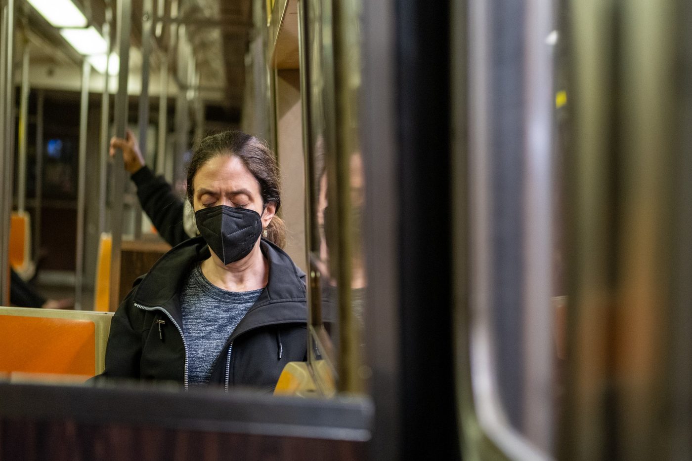 Masked female passenger with closed eyes gripping the subway pole, New York