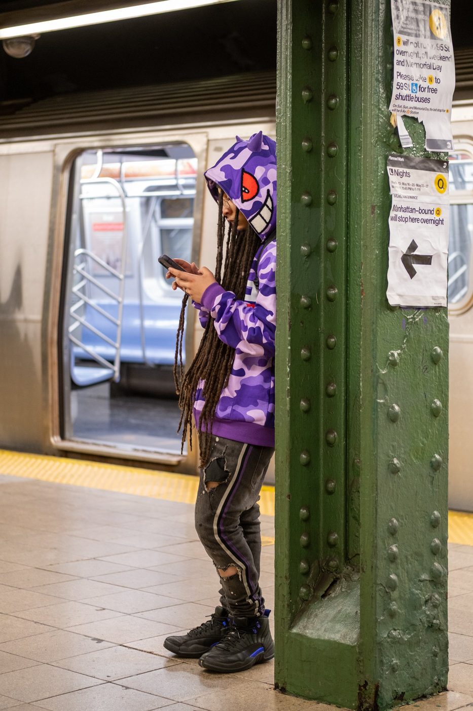 Teenager in a monster-print sweatshirt absorbed in his phone on the platform, New York