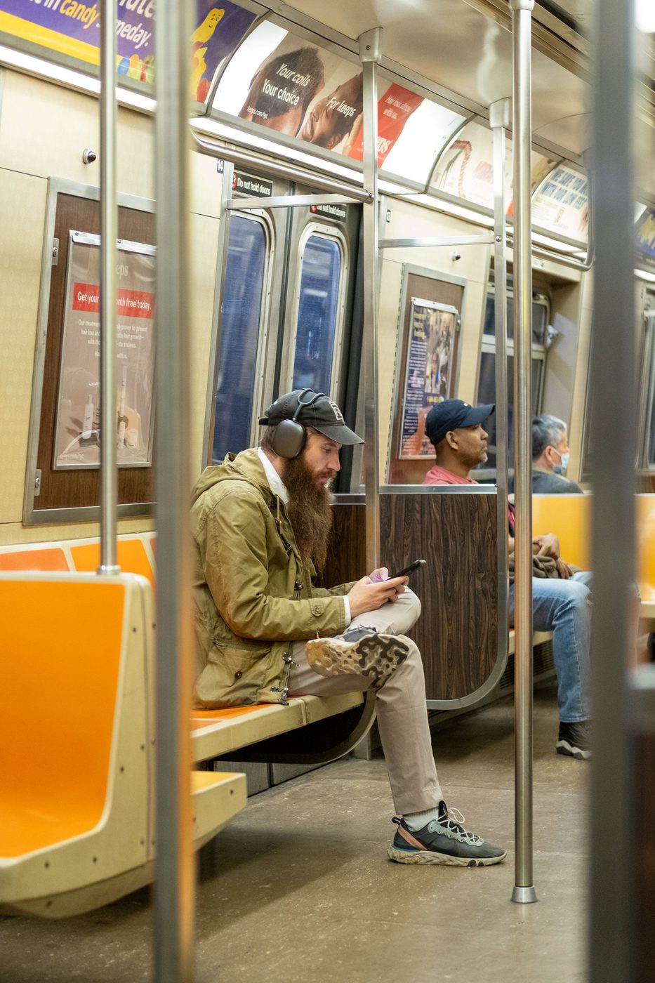 Bearded man wearing a helmet sitting on the subway, absorbed in his phone, New York