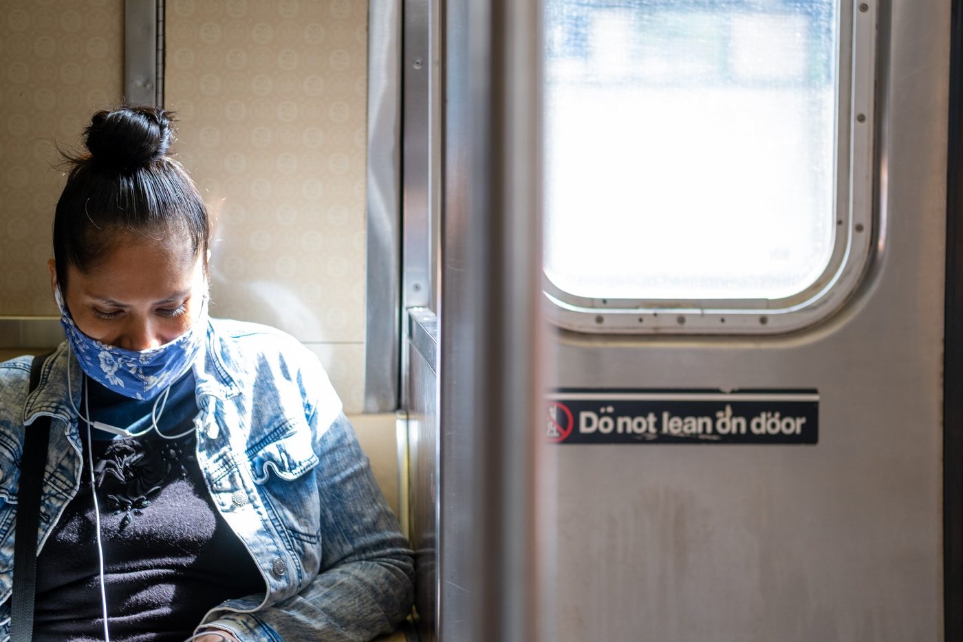 Female passenger with a bun and floral mask sitting near a subway door, New York
