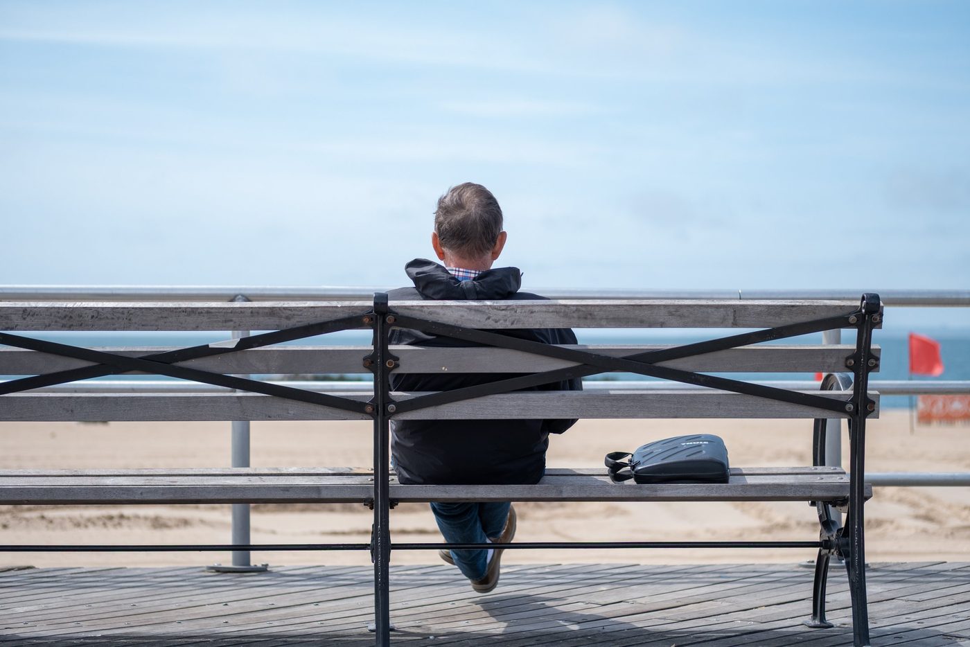 Man seen from behind sitting on a bench facing the ocean, New York