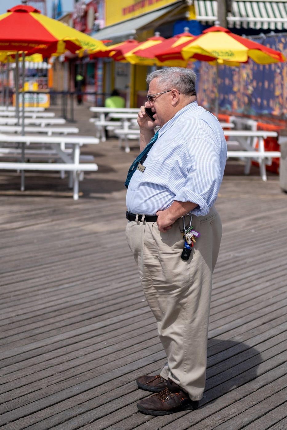 Man on the phone on the boardwalk lined with red and yellow parasols, New York