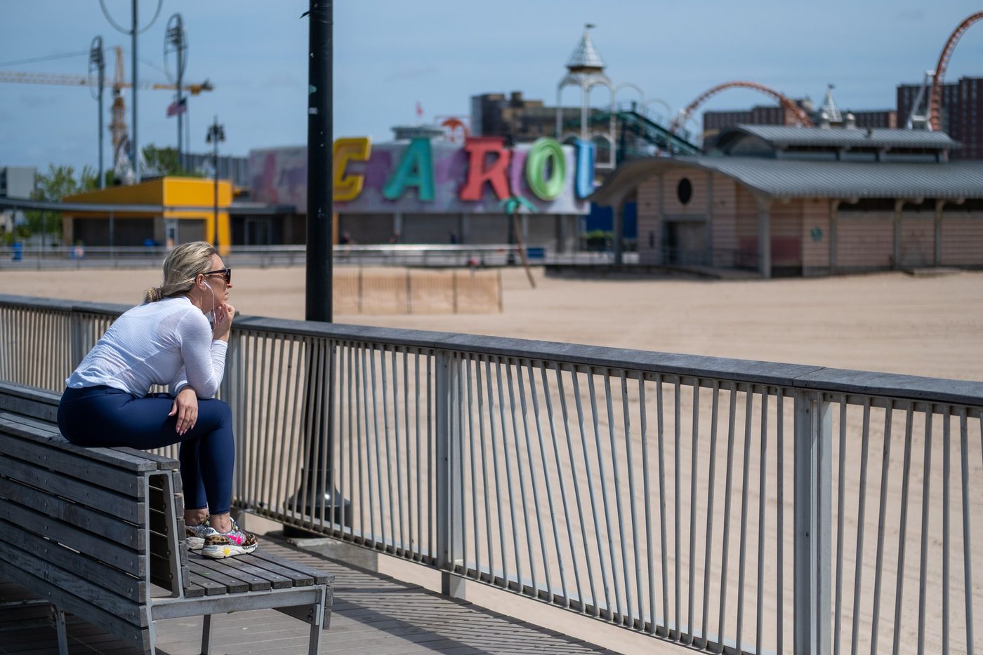 Woman sitting on a railing facing the beach and the Coney Island carousel, New York