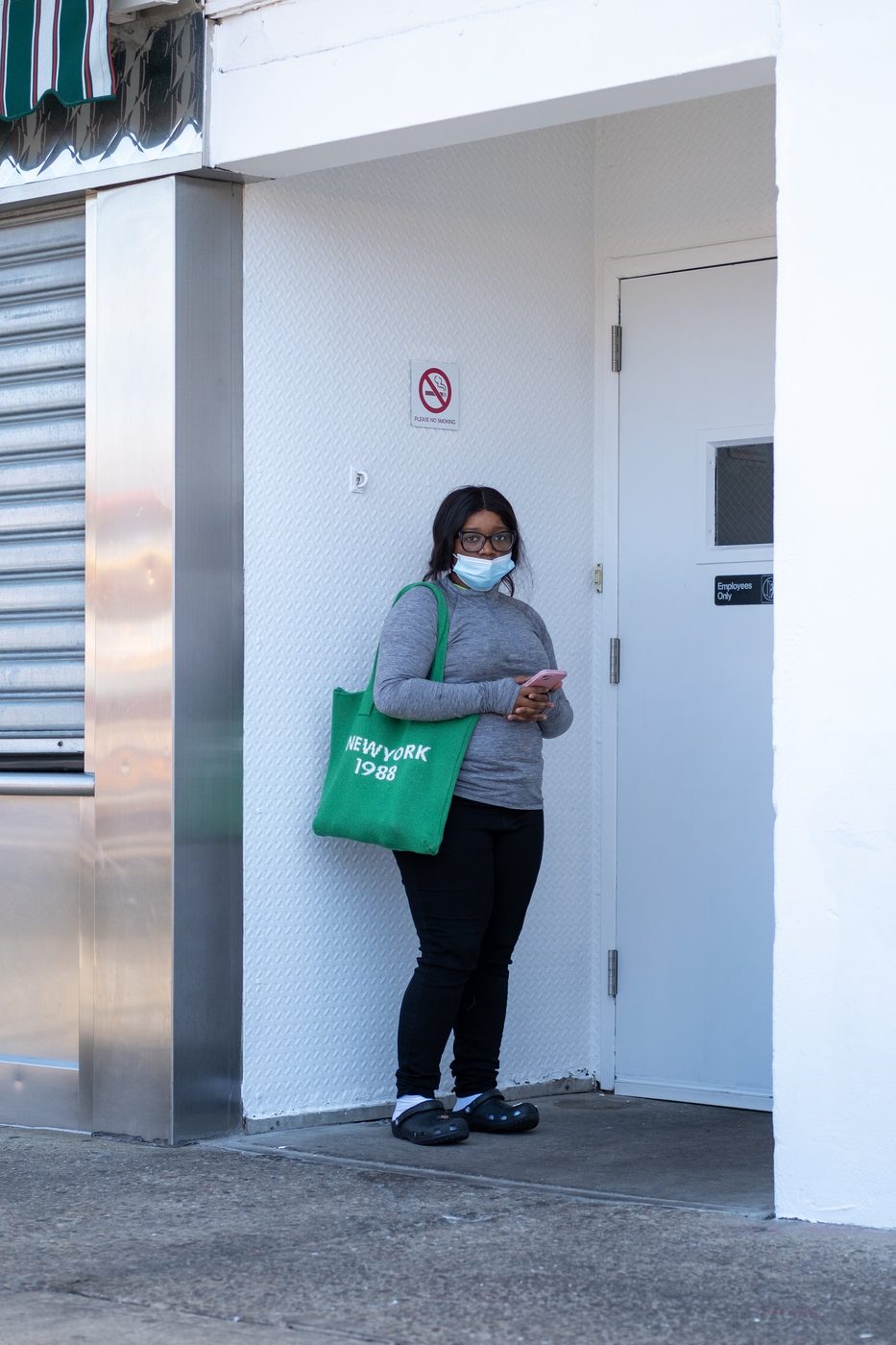 Masked woman with a New York 1988 tote bag in front of a doorway, New York