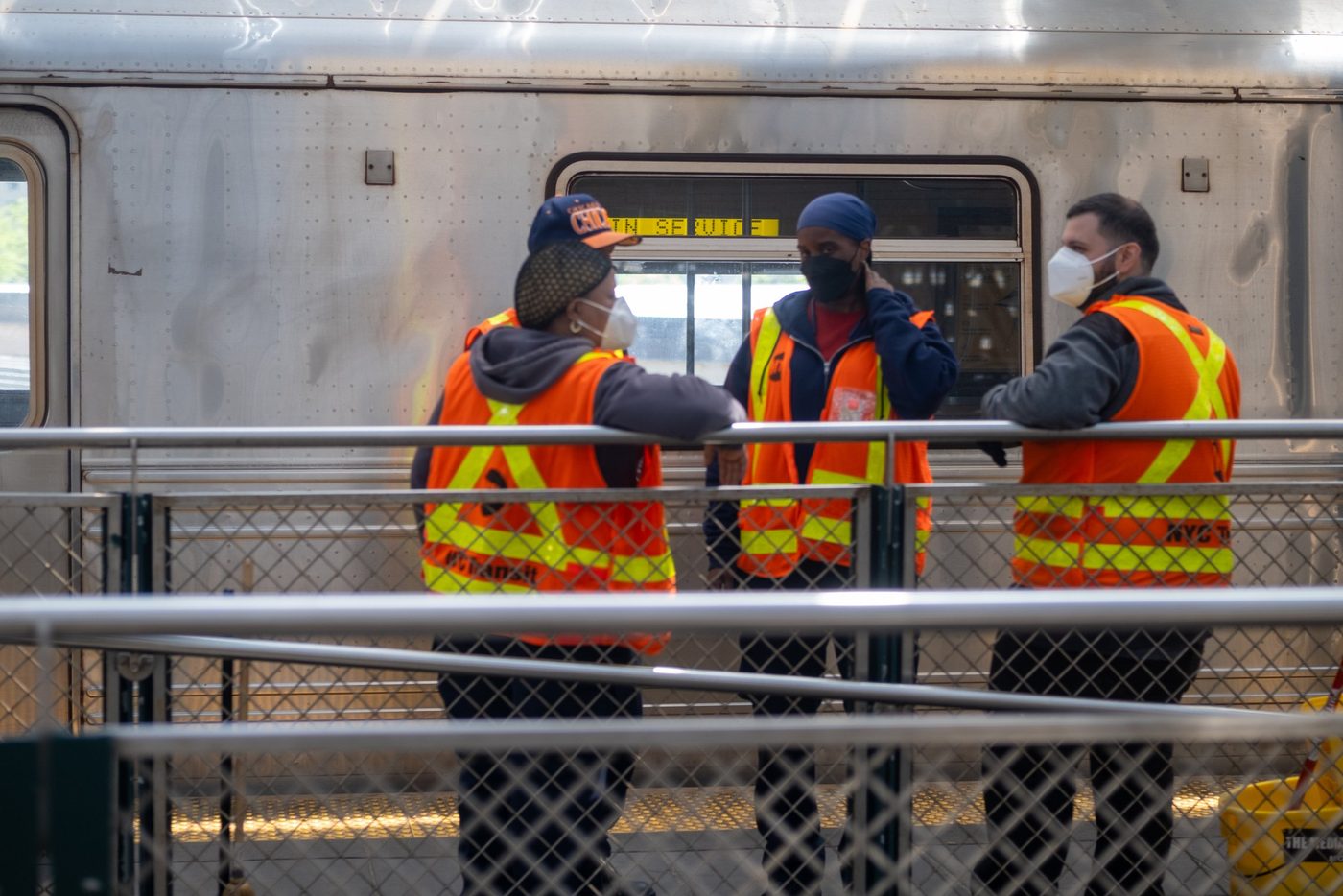 Three workers in fluorescent orange vests chatting in front of a subway car, New York