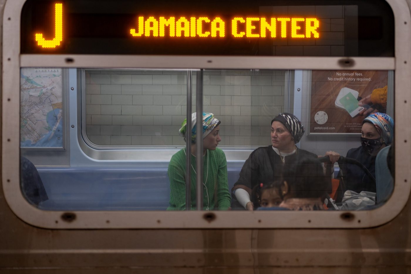 Female passengers in headscarves and a child seen through the window of the Jamaica Center train, New York