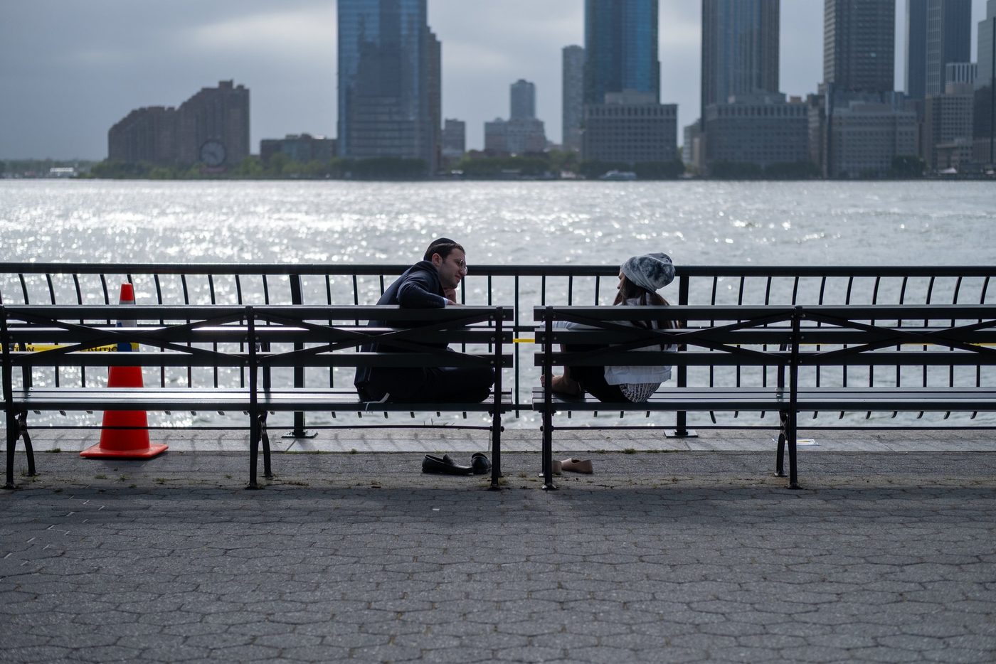 Couple sitting back to back on benches facing the river, skyline in the background, New York