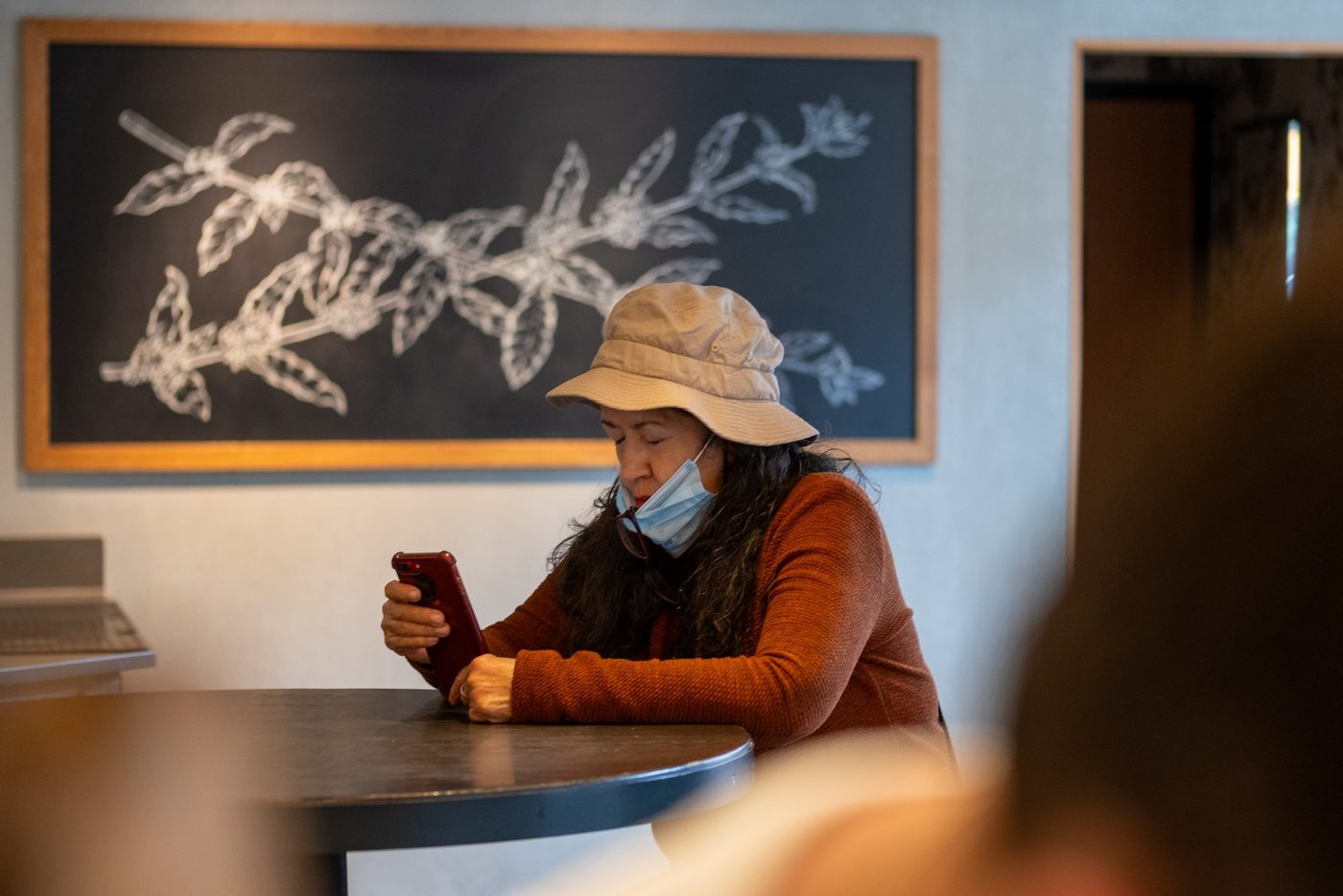Woman in a hat and mask checking her phone in a cafe, New York