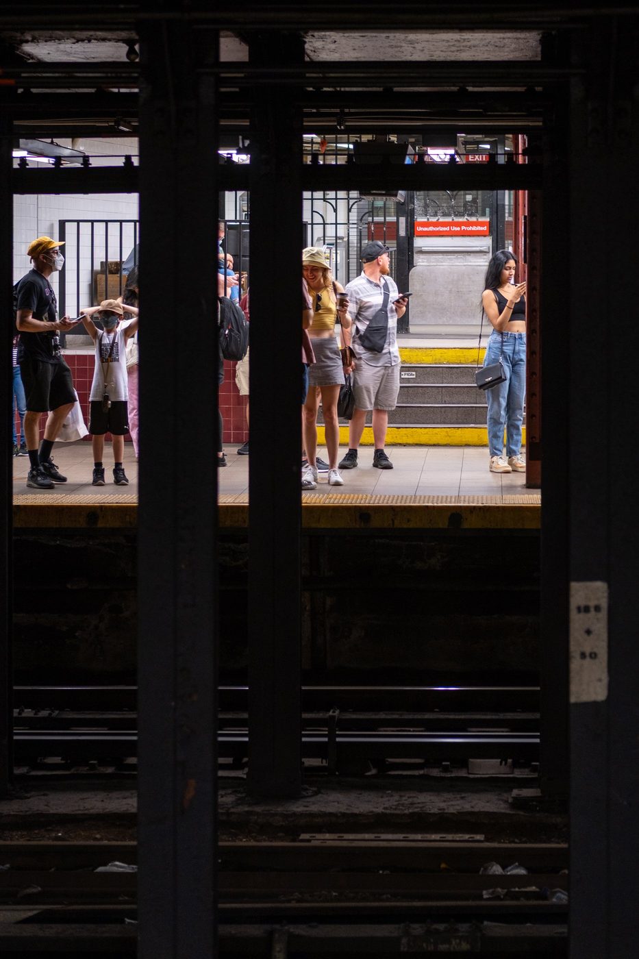 Travelers waiting on the platform seen between the subway's steel beams, New York