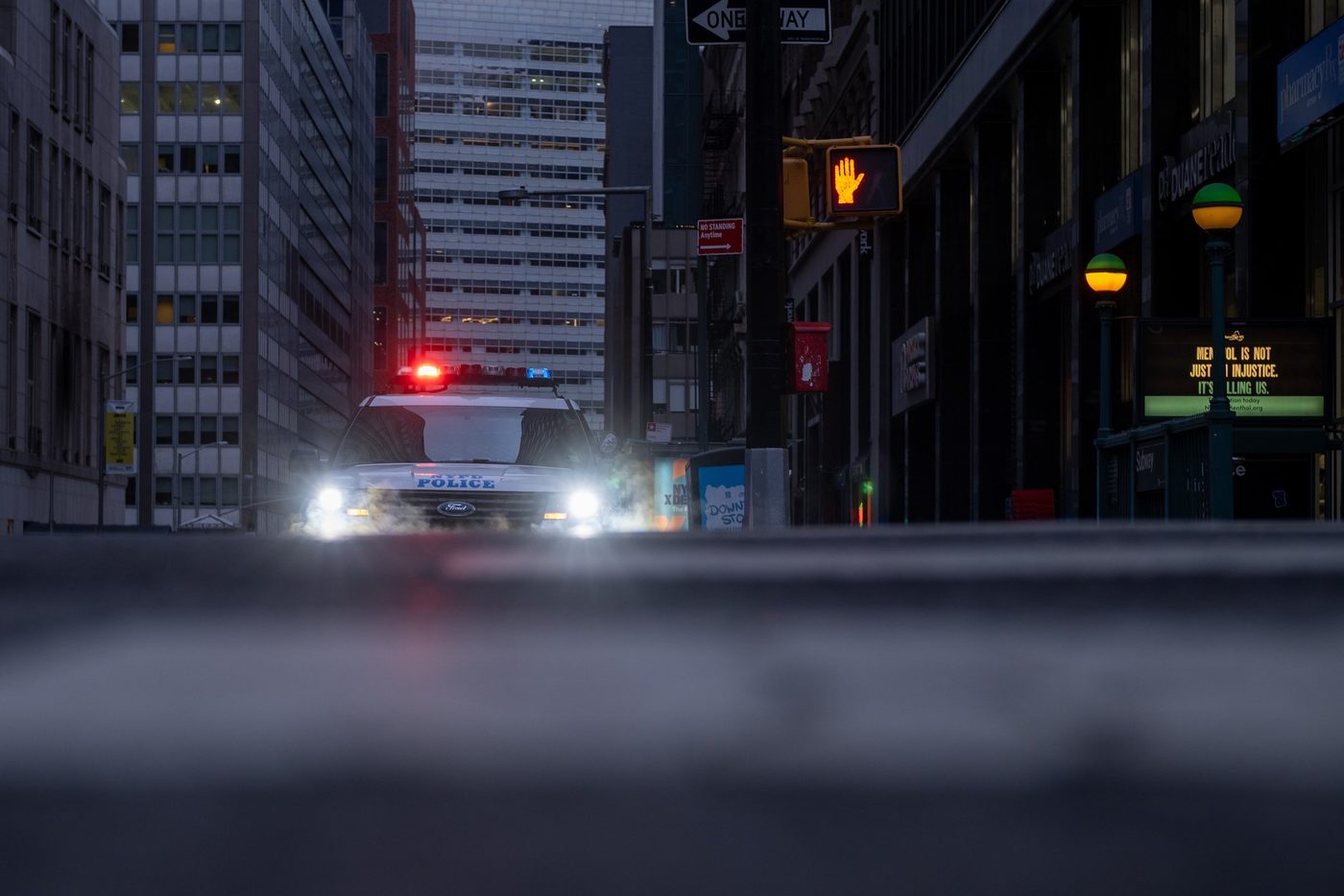 Police vehicle driving with lights on down a street at dusk, New York
