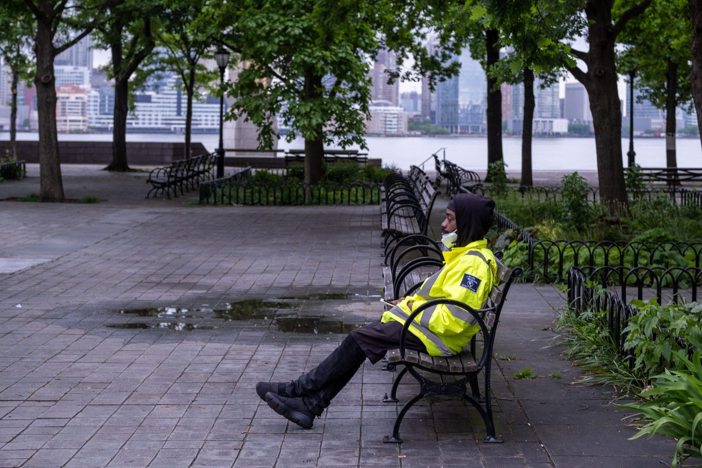 Worker in a fluorescent yellow vest sitting on a bench facing the river, New York