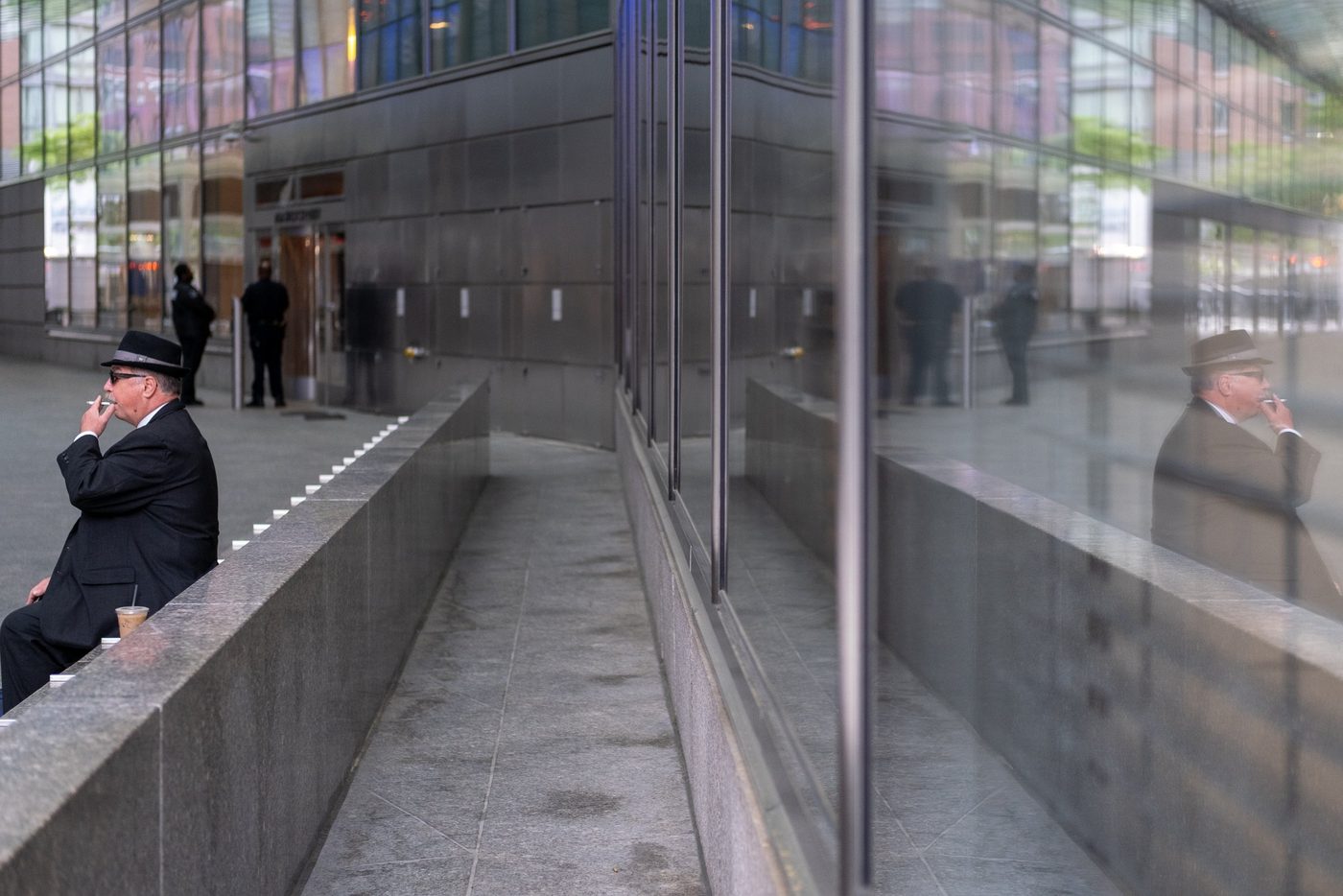 Man in a hat smoking a cigarette, reflected in a glass wall, New York