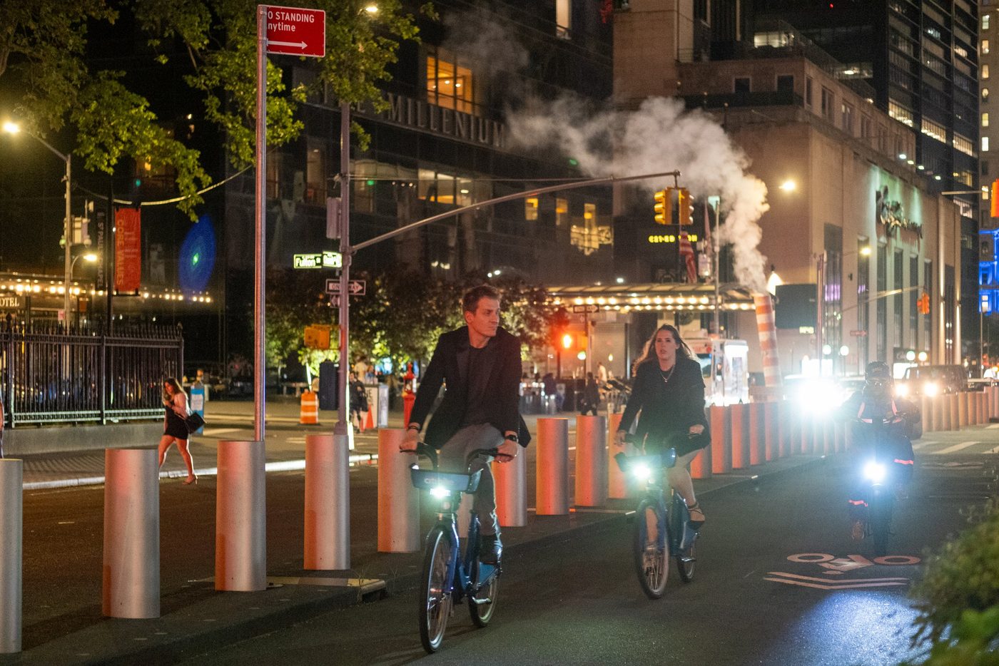 Two cyclists on Citi Bikes riding at night near a steam vent, New York