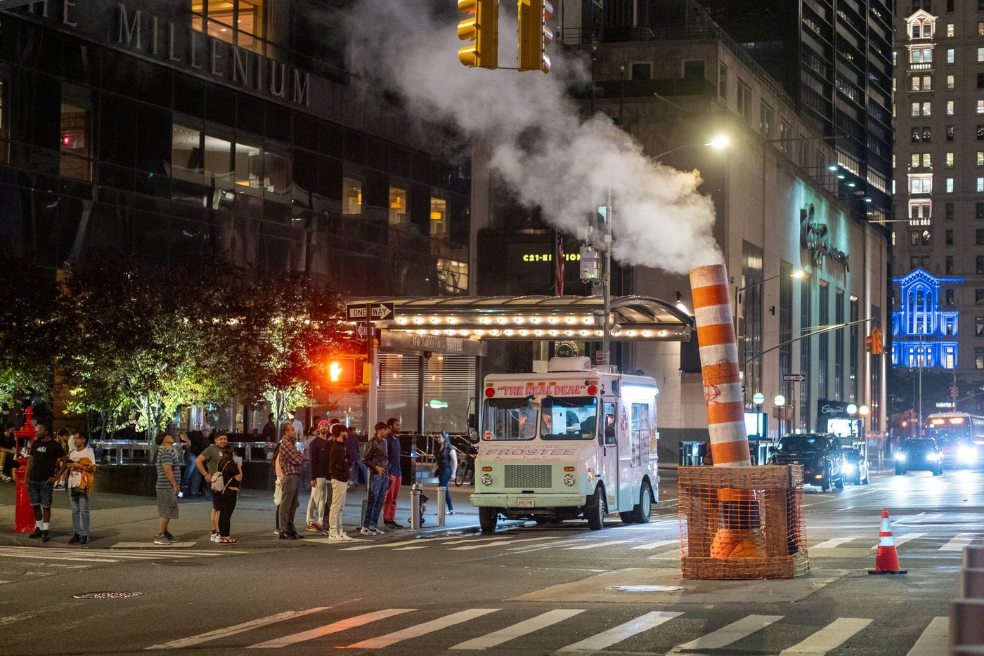 Ice cream truck lit up at night in front of a line of customers, New York
