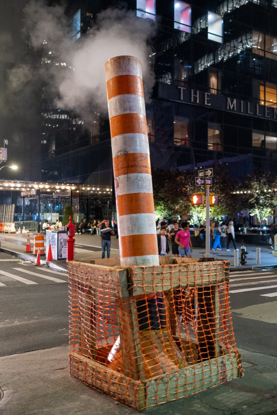 Orange-and-white striped construction chimney spewing steam at night, New York