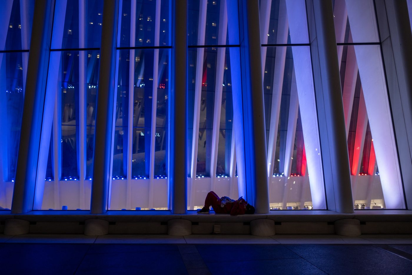 Person lying at the foot of the Oculus's illuminated ribs at night, New York