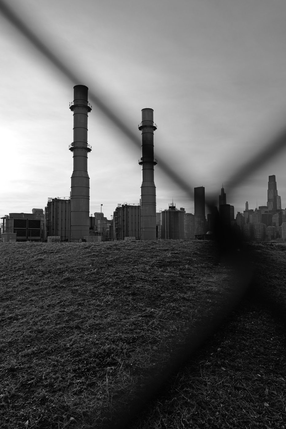 Industrial smokestacks seen through a chain-link fence, skyline in the background, New York