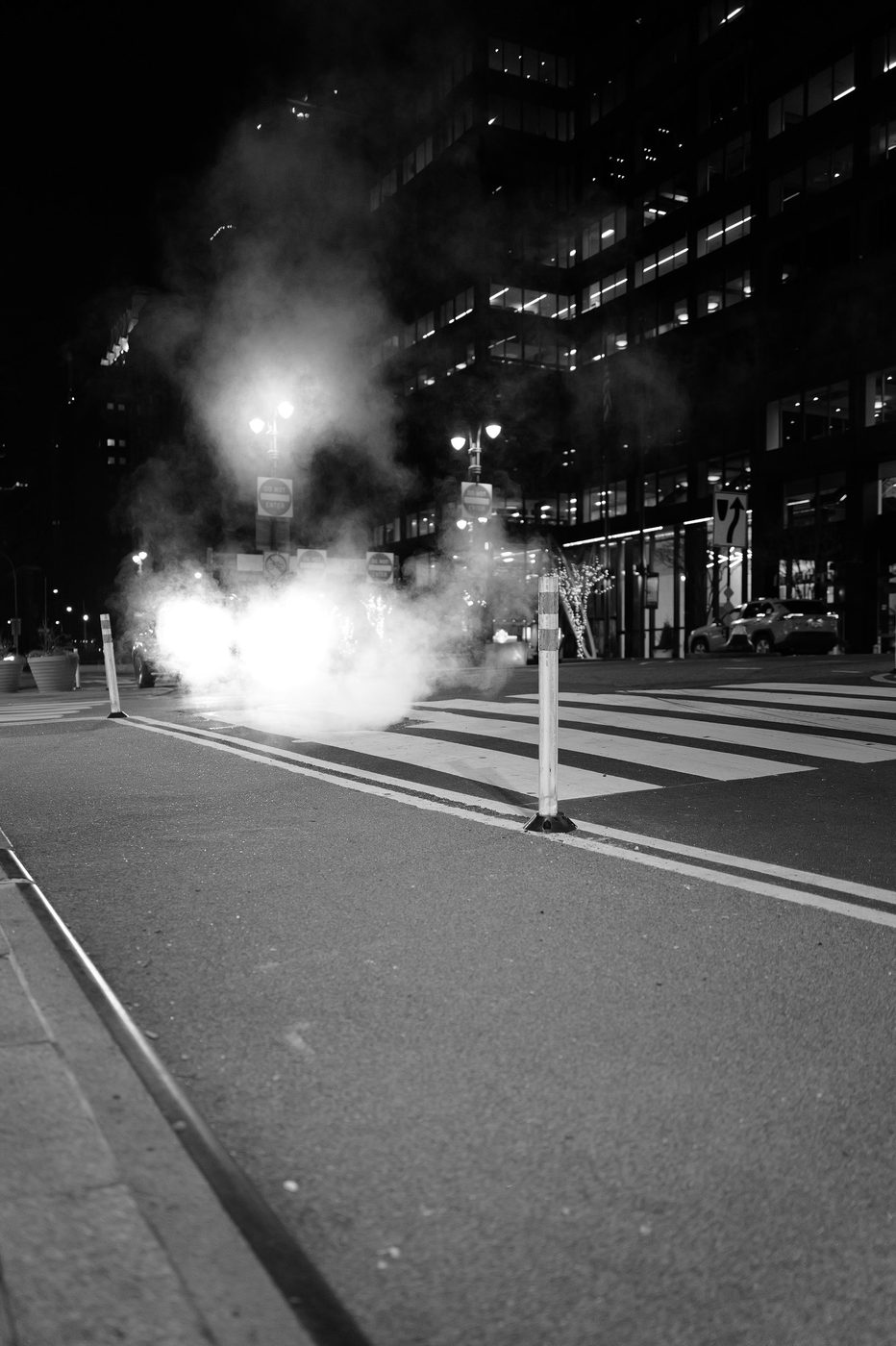 Steam lit up by headlights in the middle of a crosswalk at night, New York
