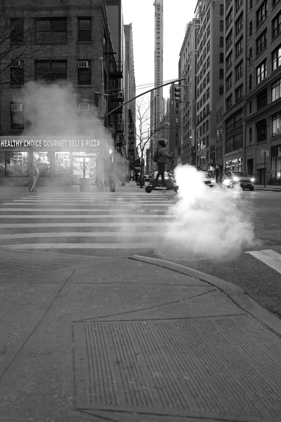 Delivery rider on a scooter crossing the street near a steam vent, New York