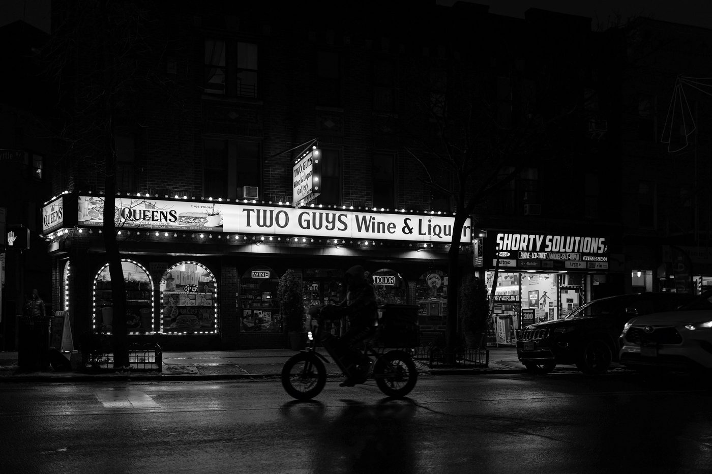 Delivery cyclist passing the Two Guys Wine & Liquor sign at night, New York