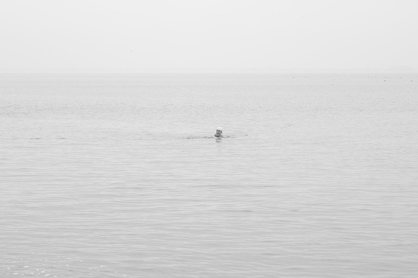 Swimmer in the distance in a still, milky sea, New York