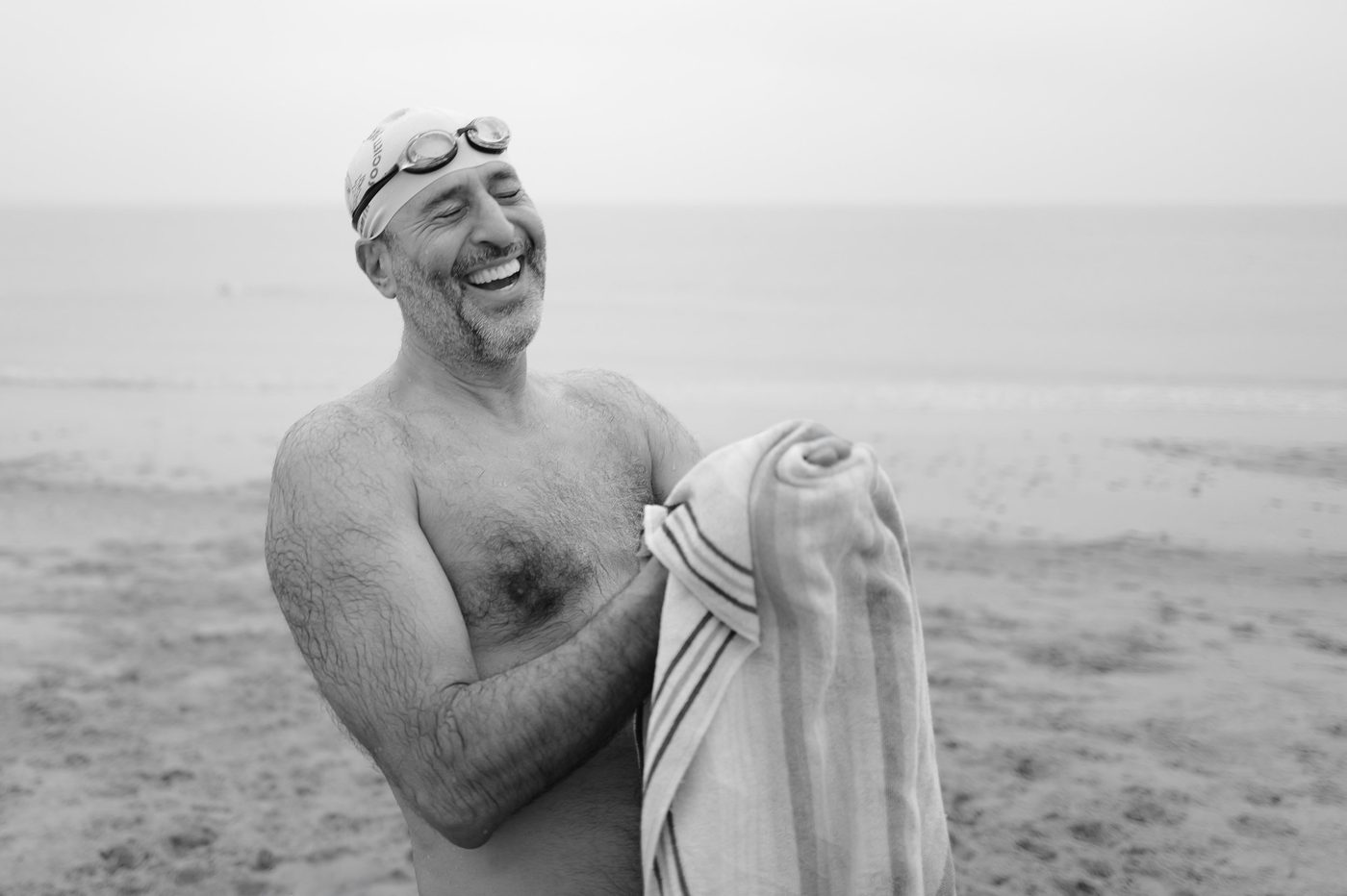 Man laughing heartily in a swim cap, towel in hand, New York