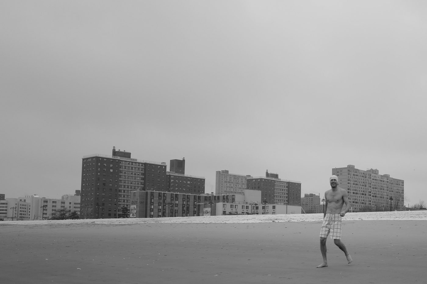 Smiling man walking barefoot on the beach, buildings in the background, New York