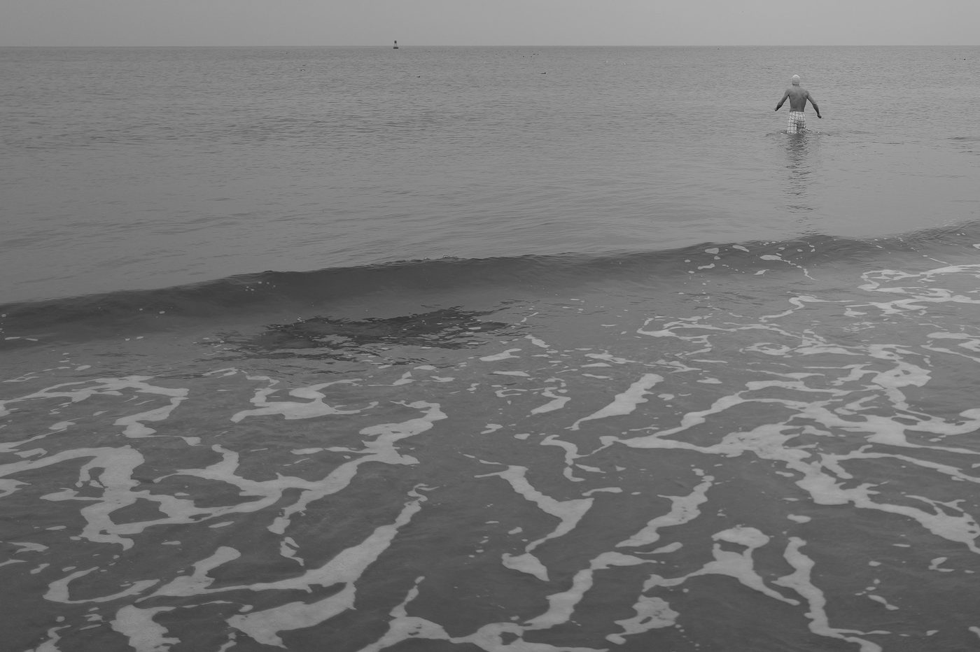 Swimmer wading into the sea, foam patterns in the foreground, New York