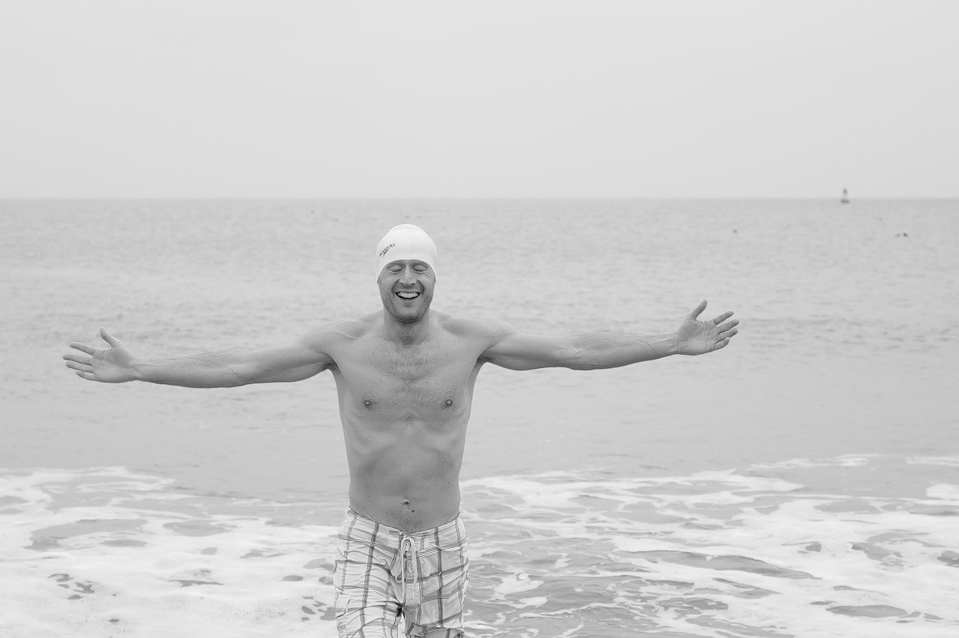 Close-up portrait of a laughing swimmer with arms open facing the sea, New York