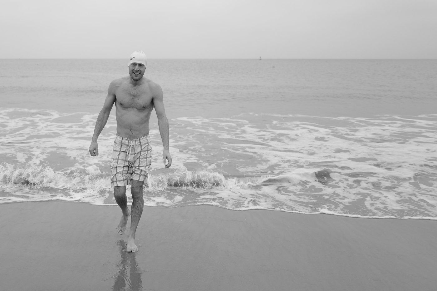 Smiling man coming out of the water and walking toward the beach, New York