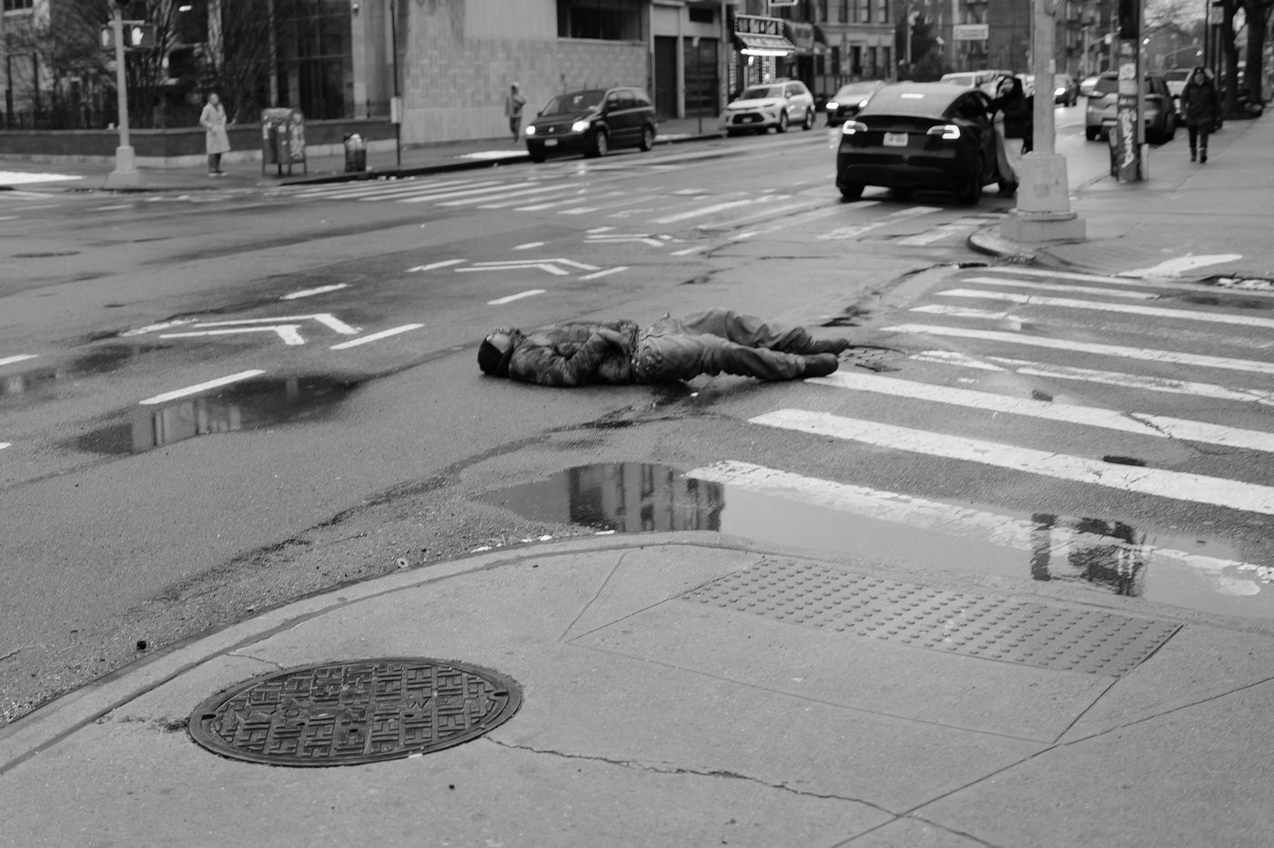 Person lying on the road at an intersection, cars around, New York
