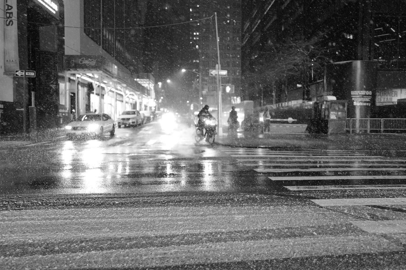 Motorcyclist crossing an intersection during a nighttime snowfall, New York