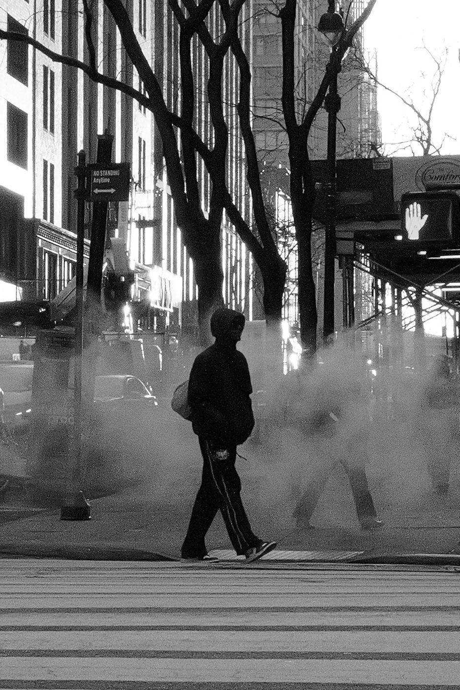 Silhouette crossing the street among blurred passersby in the steam, New York