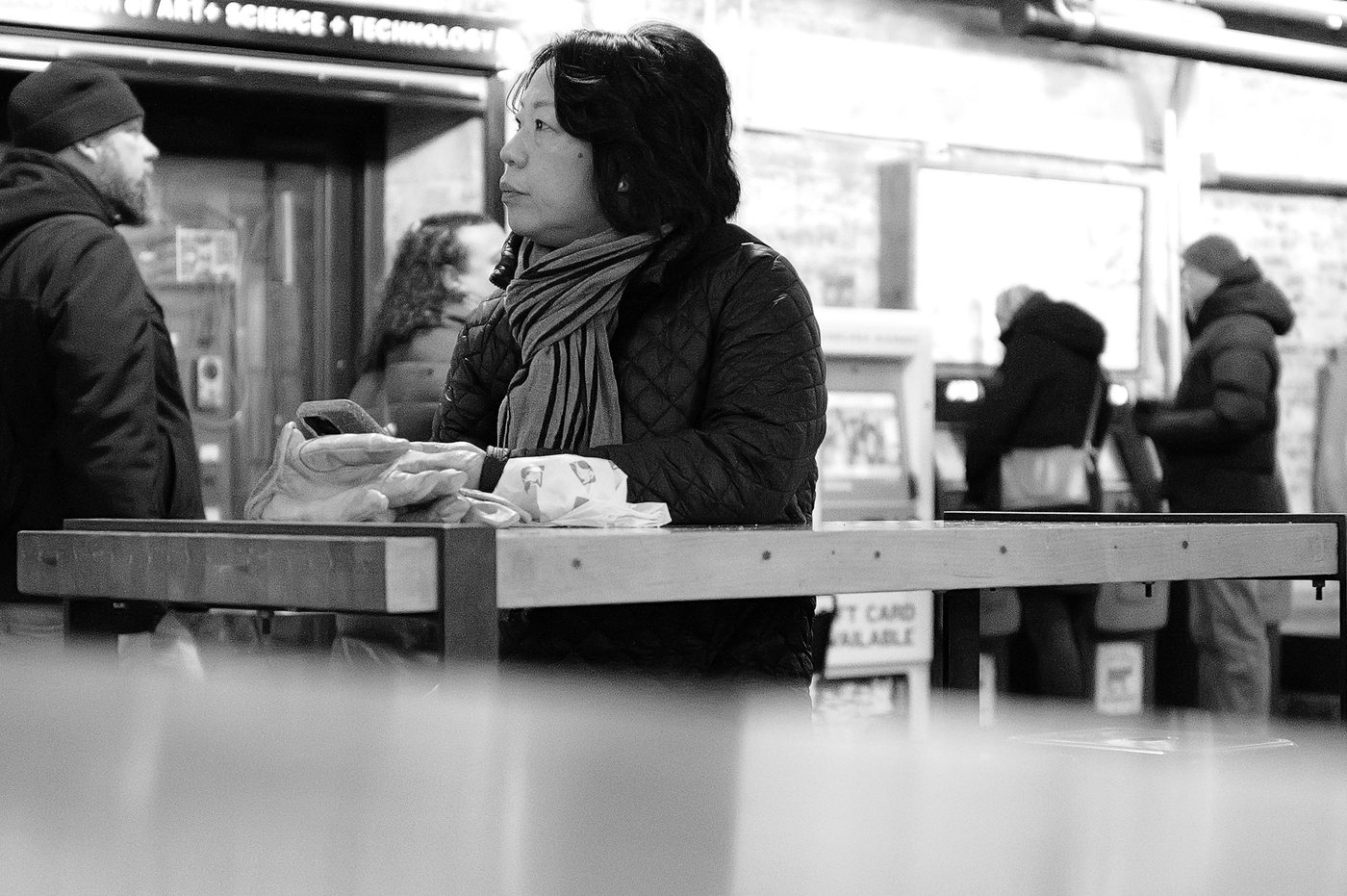 Woman in a scarf leaning on a counter, phone in hand, New York
