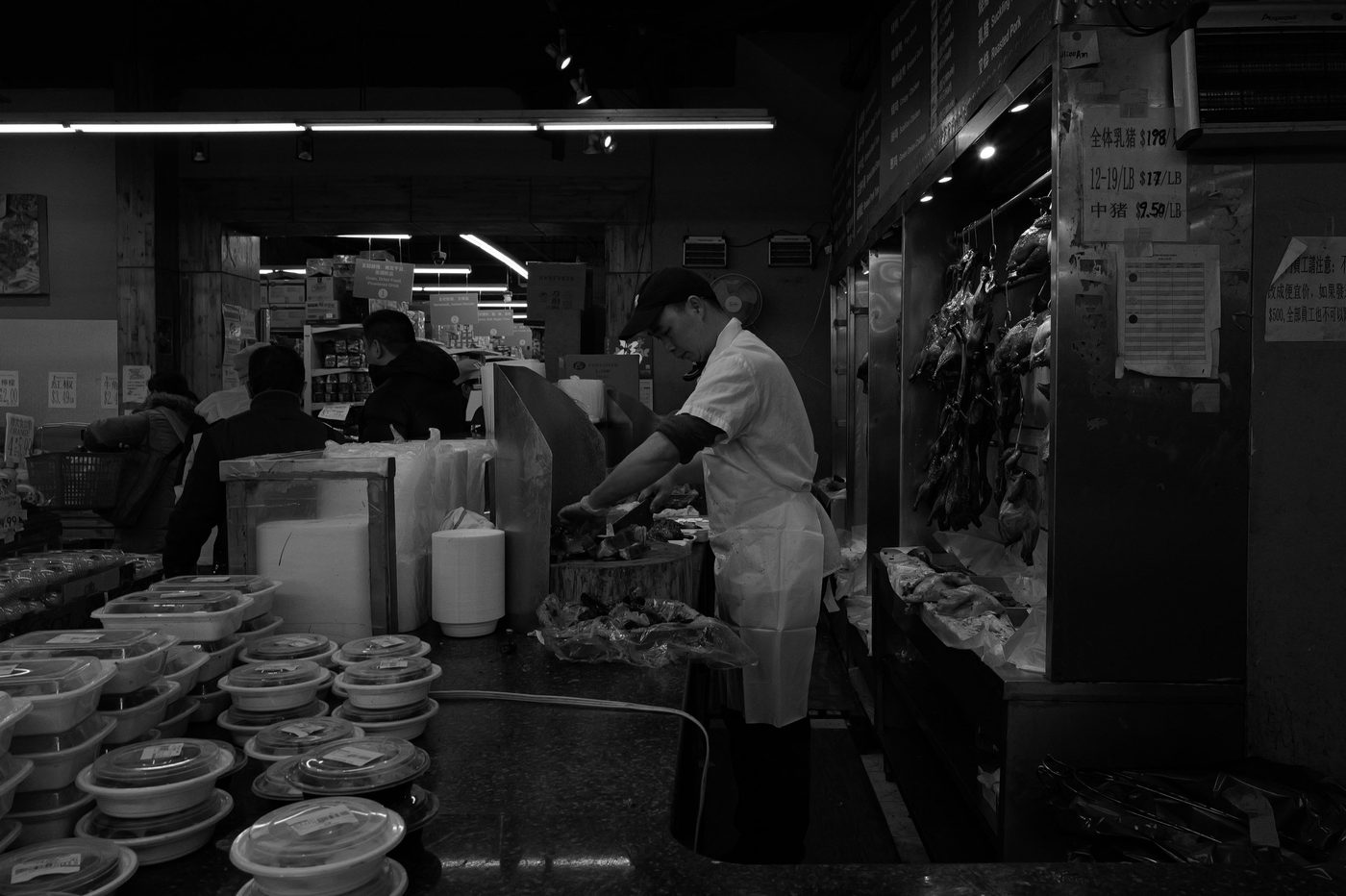 Butcher working beneath glazed ducks hanging in the window, New York