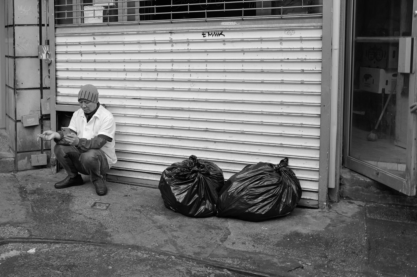Man crouching, smoking a cigarette near trash bags, New York