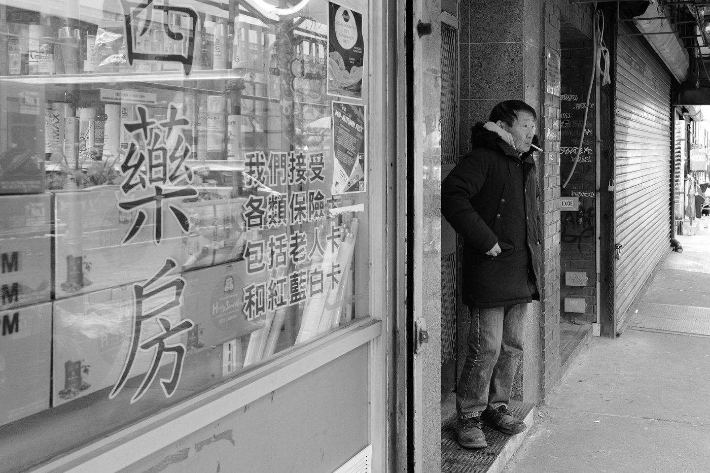 Man smoking a cigarette in the doorway of a Chinese pharmacy, New York
