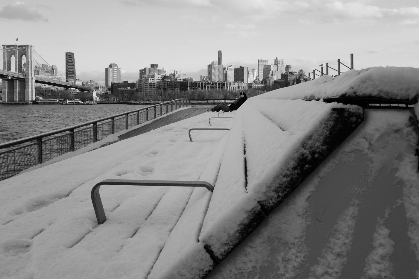 Snow-covered benches on a pier facing the Brooklyn Bridge, New York