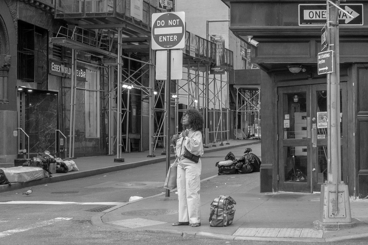 Woman waiting under a Do Not Enter sign, luggage set on the ground, New York