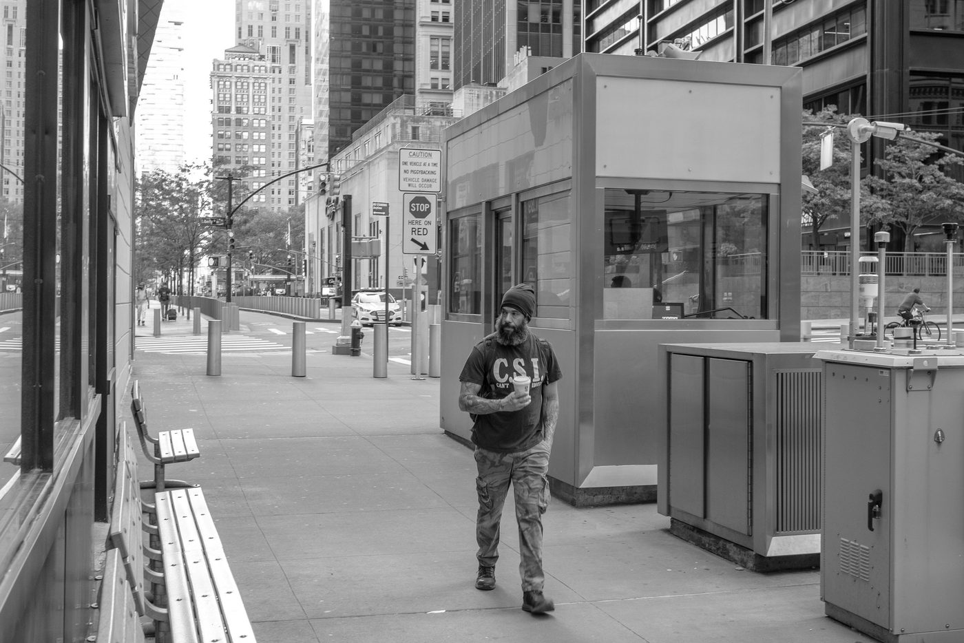 Bearded man holding a coffee walking past a security post, New York
