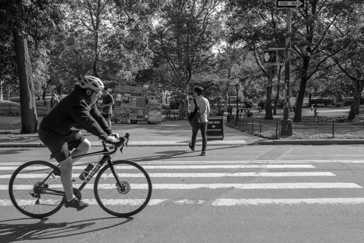 Cyclist crossing a Central Park path near a hot dog cart, New York