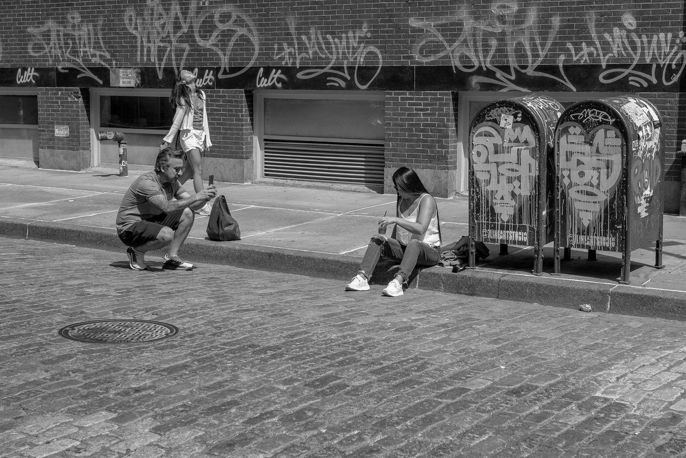 Three friends photographing tagged mailboxes on a cobblestone street, New York