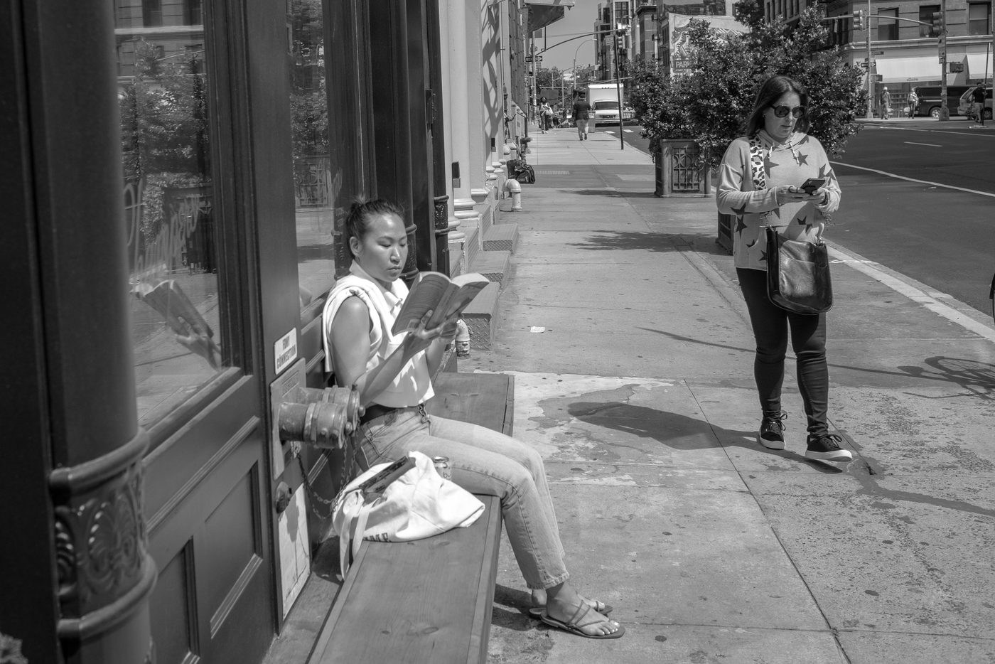 Woman reading a book on a bench, a woman on her phone nearby, New York